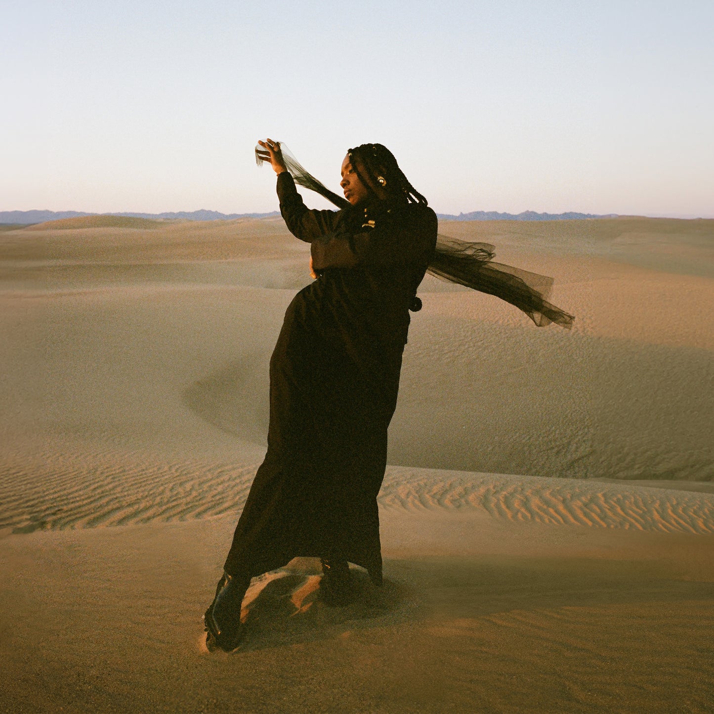Woman in black flowing dress dancing on sand dunes at sunset for Of Earth & Wires vinyl album cover