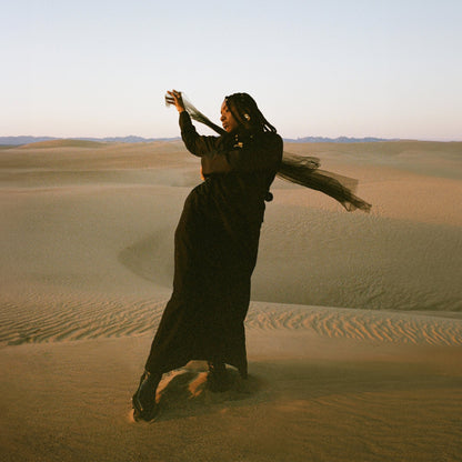 Woman in black flowing dress dancing on sand dunes at sunset for Of Earth & Wires vinyl album cover